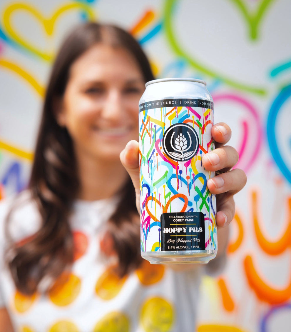 Person holding a colorful beer can in front of a multicolored heart-patterned background
