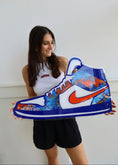 Load image into Gallery viewer, Woman holding a large inflatable sneaker with a colorful design and Nike logo.
